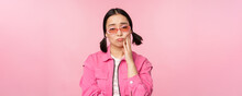 Image Of Sad Asian Girl Sulking, Touching Her Cheek, Pouting Disappointed, Has Toothache, Standing Over Pink Background