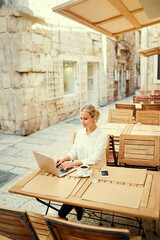 Wall Mural - Technology and travel. Working outdoors. Freelance concept. Pretty young woman using laptop in sidewalk cafe on ancient europian street.