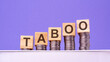 wooden cubes with the word Taboo on money pile of coins, business concept