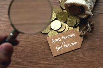 a hand holding a magnifying glass pointing to a bag of gold coins with a tag written with gross inco