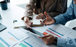 © Natee Meepian - Close up two business partnership coworkers discussing a financial planning on digital tablet and paperwork.