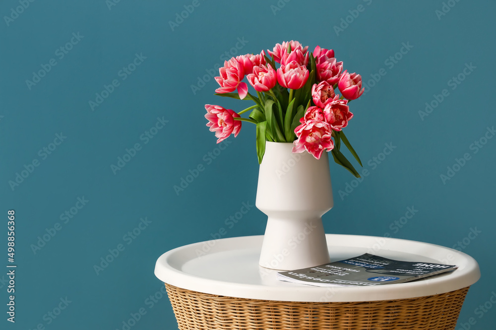 Vase with tulips and magazine on table near color wall