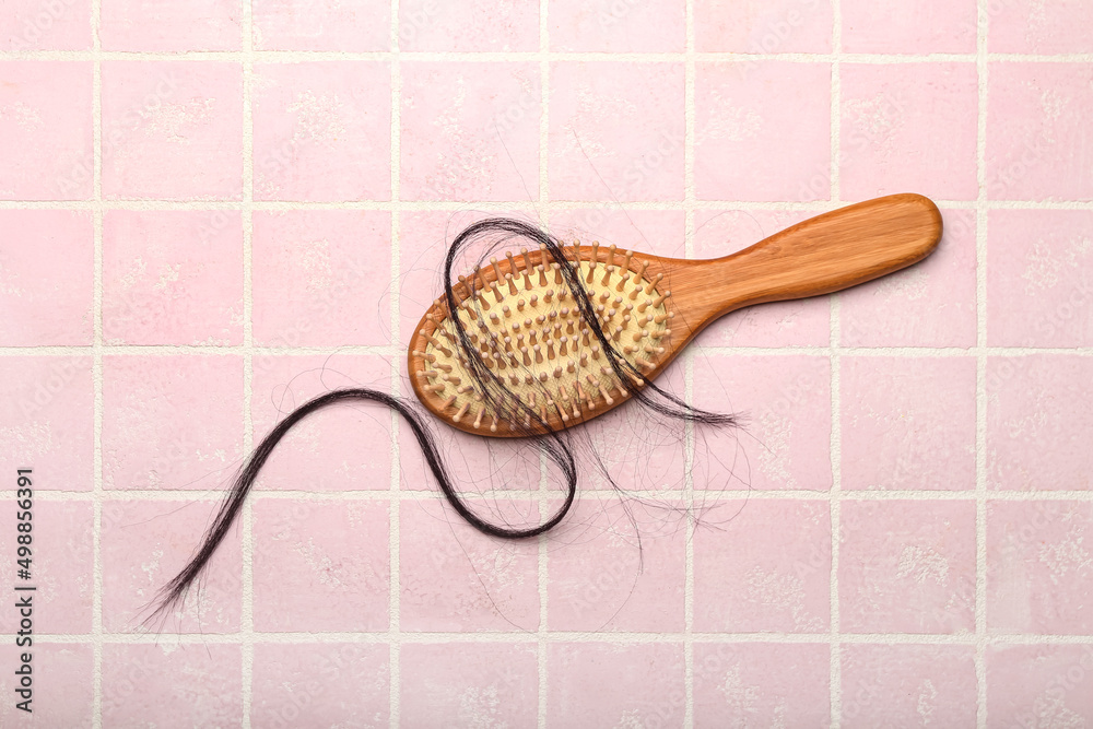 Brush with fallen down hair on pink tile background