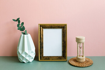 Wall Mural - Blank picture frame, vase of plant, sandglass on green table. pink wall background. home interior