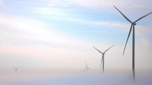 Silhouettes Of Windmills With Large Propellers Operating At Offshore Station. Contemporary Turbines Generate Green Electric Power In Foggy Morning
