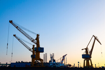  Silhouettes of harbor cranes at sunset. Shipyard at sunset.