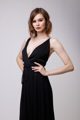 Wall Mural - High fashion photo of a beautiful elegant young woman in a pretty black evening party dress with a deep neckline posing on white background. Slim figure, hairstyle, studio shot. 
