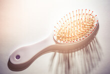 Selective Focus Of White Plastic Hairbrush On White Isolated Background. There Are Long Strands Of Hair Between The Combing Ends Of The Brush.The Shadow Of The Comb Tips Of The Brush Is On The Ground.