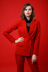 Wall Mural - High fashion photo of a beautiful elegant young woman in a pretty red suit, jacket, pants, trousers, black blouse posing on background. Slim figure, hairstyle, studio shot. Monochrome, total red