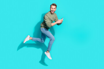 Poster - Full length photo of cheerful influencer man jump hold telephone run wear pullover isolated blue color background