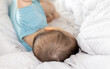 © Alexandra - cute baby boy in blue bodysuit is laying on bed, on white blanket. child is feeling protected, relaxed and calm. adorable toddler is staying home. motherhood, baby care concept.