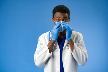 Wall Mural - Confident black doctor in face mask and gloves in blue studio