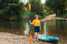 World Tourism Day. A Young Happy Woman Stands With An Oar In Her Hand Near The Kayak. The Concept Of Kayaking And Outdoor Activities