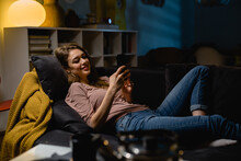 Woman Is Using Mobile Phone And Relaxing On A Sofa At Home