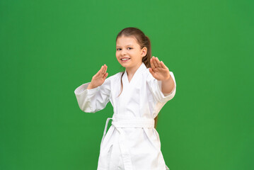 Poster - a little girl in a white kimono does a warm-up before training on a green background. child is studying martial arts