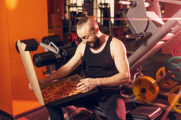 A bearded man in the gym opens a pizza box