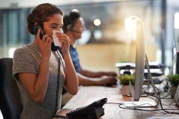 Poster - Dont delay going to the doctor when youre ill. Shot of a young businesswoman blowing her nose while talking on a phone in an office.