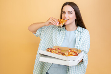 Wall Mural - Happy young woman holding hot pizza in box and bites piece of pizza