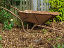 An Old Wheelbarrow Now Without Its Wheel Stands Rusty And Neglected Outside A Garden Allotment
