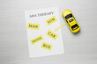 Taxi car model and paper sheet with phrase ABA Therapy on white wooden table, flat lay