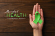 World Mental Health Day. Woman holding green ribbon at wooden table, top view
