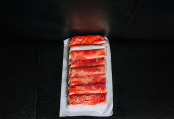 A large package of frozen crab sticks, fish meat lies on a black background. Food photography, concept.