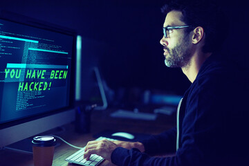 Fototapete - He could be coming for you. Shot of a focussed computer hacker using a computer in the dark.