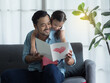 Handsome Dad and cute girl reading gift card with love and happiness. Little daughter hugging father from backside after giving card and gift to father.