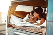 © Nikish H/peopleimages.com - Anywhere is better together. Shot of two happy friends relaxing on a blanket in the true of their van on a road trip.