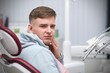 Portrait of young guy, handsome frightened man is suffering from strong teeth or tooth pain in dental office at clinic lying, having a seat in medical chair after dentist treatment holding his cheek