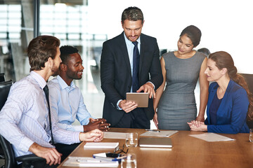 Canvas Print - Running the numbers past his team. Shot of a group of corporate colleagues talking together over a digital tablet in an office.