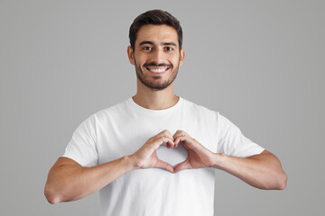 Wall Mural - Portrait of smiling young man keeps hands on chest in heart shape sign