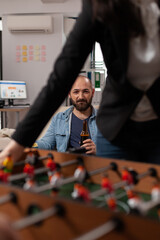 Wall Mural - Portrait of business man drinking beer from bottle at office party after hours, enjoying leisure activity with colleagues. Cheerful adult having fun with after work drinks and foosball game.