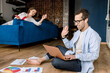 © shunevich - Image of a successful young couple waving hello to their colleagues working on laptops together while sitting at home. Happy couple good emotions have achieved success in a new project.