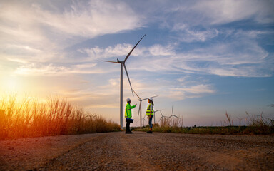 Engineer wearing uniform ,helmet hold document inspection work in wind turbine farms rotation to generate electricity energy. Green ecological power energy generation wind sustainable energy concept.