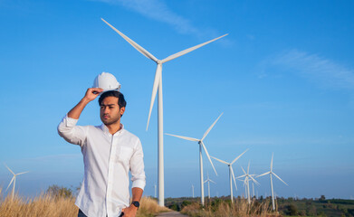 Wall Mural - Engineer wearing uniform ,helmet hold document inspection work in wind turbine farms rotation to generate electricity energy. Green ecological power energy generation wind sustainable energy concept.