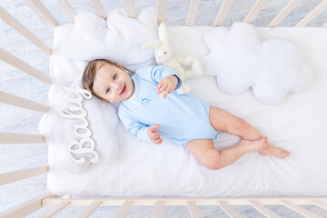 happy smiling baby boy in the crib with the inscription baby in a blue bodysuit, cute joyful little baby in the bedroom