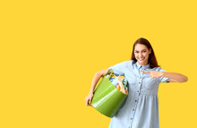 Beautiful Woman Pointing At Green Basket With Laundry On Yellow Background
