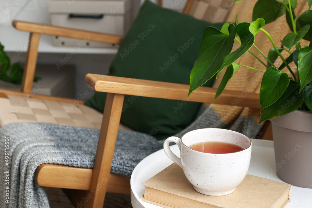 Cup of tasty tea with book on table in room