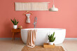 Modern bathtub with towel and houseplants near brown wall