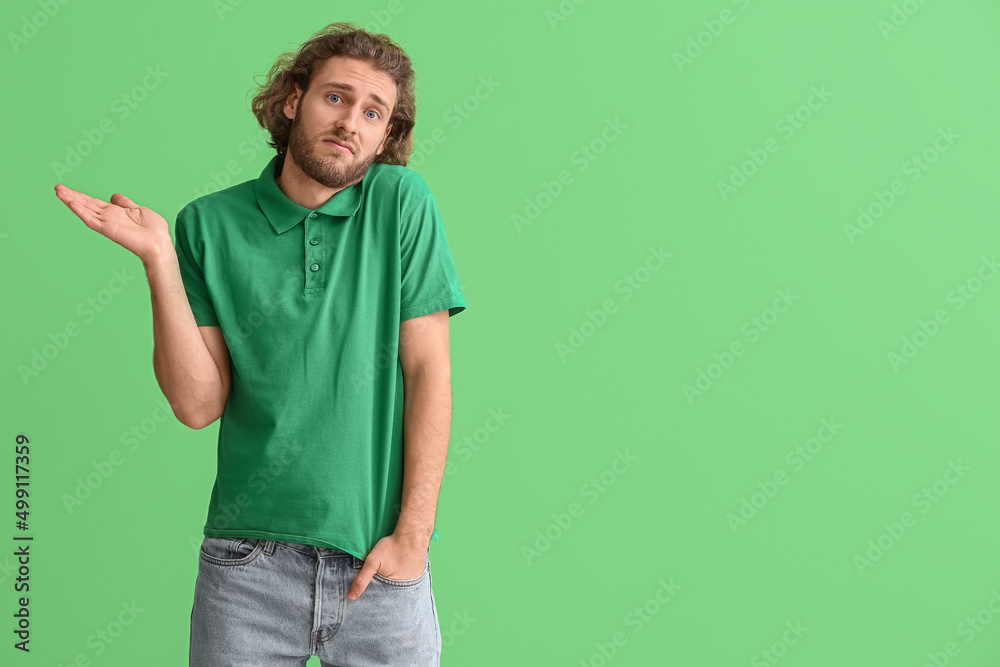 Handsome man in t-shirt shrugging on green background