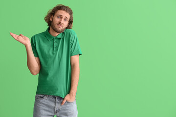 Wall Mural - Handsome man in t-shirt shrugging on green background