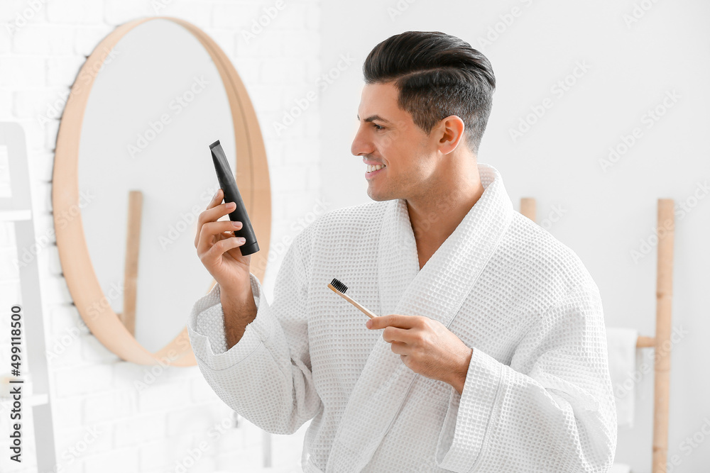 Handsome young man with activated charcoal tooth paste and brush in bathroom