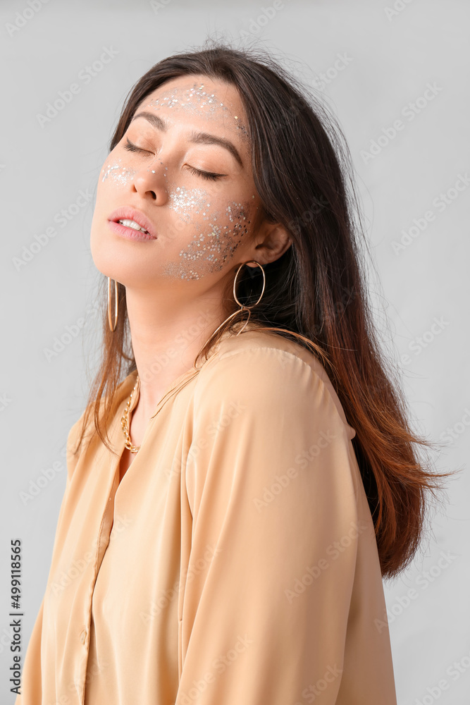 Asian woman with glitter makeup and closed eyes on light background