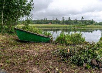 Wall Mural - lake shore and boat, calm lake water surface, tree reflections, cloudy day, fishing concept