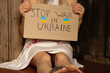 A Ukrainian girl in a white dress with blood stains on her dress, tortured by Russian soldiers in the corner of the room, holds a sign with the text stop the war in Ukraine