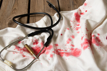 A stethoscope and a bullet lie on a dress with red blood stains, traces of blood on things and a bullet wound, medical assistance