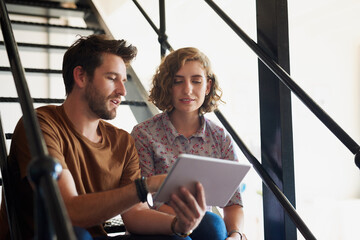 Poster - What could we modify to create more value. Shot of two designers discussing something on a tablet while sitting on a staircase.