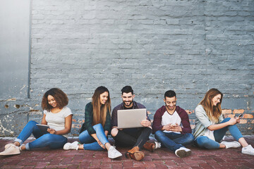 Aufkleber - Connecting in a connected era. Shot of a group of young friends using their wireless devices together outdoors.