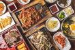 Overhead Korean bulgogi barbecue flat lay view of a dinner feast with multiple bowls and platters of beef, pork, and side dishes.